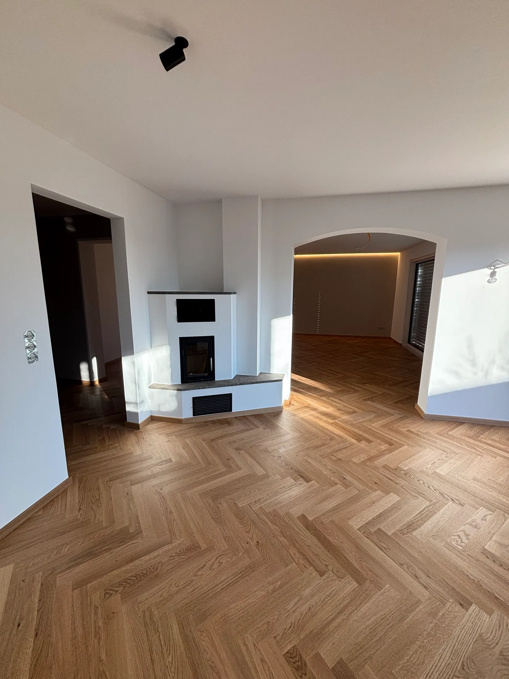 Renoviertes Wohnzimmer mit greige gestrichenen Wänden, Eckkamin und Rundbogen-Durchgang